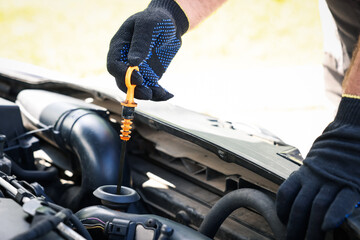 Worker checking motor oil level in car with dipstick, closeup