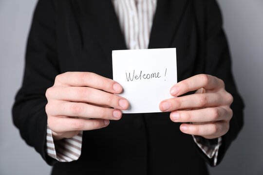 Human resources manager holding sticky note with word Welcome on grey background, closeup