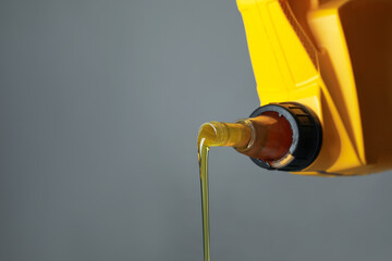 Pouring motor oil from yellow canister on grey background, closeup. Space for text