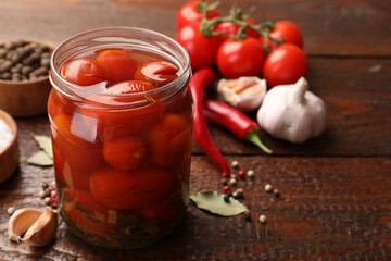Tasty pickled tomatoes in jar and ingredients on wooden table, closeup