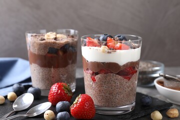 Delicious chocolate puddings with chia seeds, nuts and berries in glasses on grey table, closeup