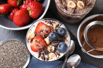 Delicious chocolate puddings with chia seeds, nuts and berries in glasses on grey table, flat lay