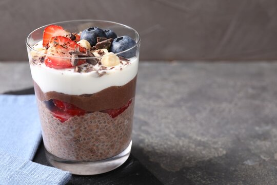 Delicious chocolate pudding with chia seeds, nuts and berries in glass on grey table, closeup. Space for text