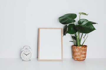 Wooden picture frame with houseplant and vintage alarm clock on the white table. Picture frame...