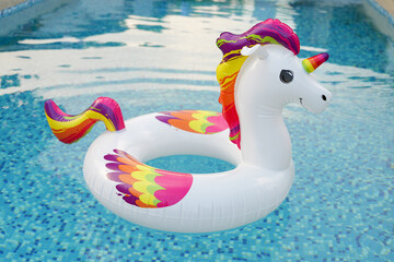 A bright, inflatable unicorn float with colorful mane and tail bobs in a shimmering blue swimming...