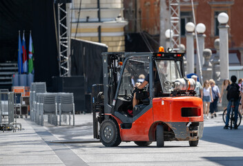 Outdoor Urban Setting with a Red Forklift Operating in a Public Square on a Clear Day with People...