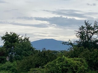 A serene scene captures Doi Suthep mountain under a cloudy sky, framed by lush green foliage,...