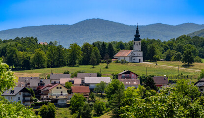 Picturesque village with a historic church surrounded by green hills and vibrant trees under a...