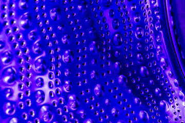 Empty washing machine drum inside in blue light, closeup view. Metal dots and bubbles as abstraction and background