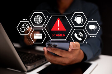 A person uses a smartphone and laptop with a digital warning sign indicating a scammer alert and...