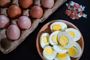A pile of halved hard boiled eggs in a wooden bowl with a few whole eggs on top of the egg carpet and egg shells