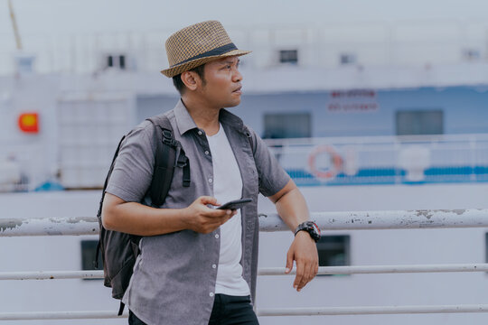 Tourist asian man backpacker enjoying solo travel vacation using cell phone on the ship. Tourism exploration and local cultural experience concept.