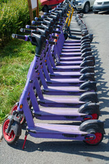 A row of parked purple electric rental scooters lined up on a city sidewalk ready for rent and urban commutes Photo