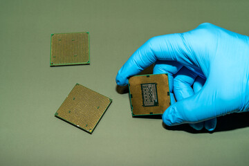 A gloved hand holds a CPU, showcasing computer technology and microchips on a green surface.