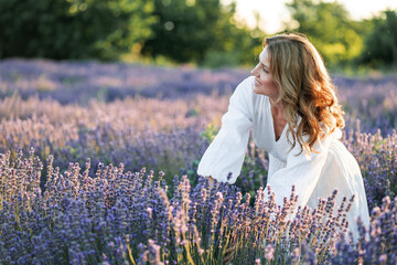 Beautiful woman enjoying summer breeze in lavender field. Portrait of blonde in sunlight....