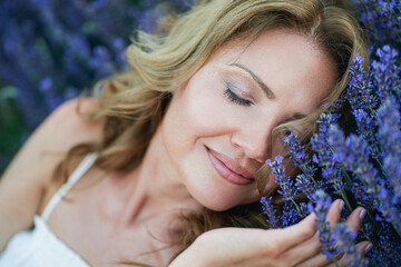 Beautiful woman enjoying summer breeze in lavender field. Portrait of blonde in sunlight....
