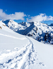 Obraz premium Majestic snowcovered mountain range under a clear blue sky, with ski tracks leading into the distance. Evokes adventure, freedom, and the beauty of winter landscapes.