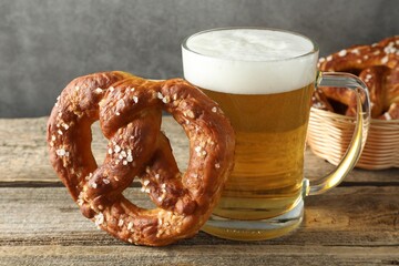 Tasty pretzel and glass of beer on wooden table against grey background, closeup