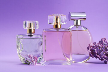 Bottles with perfumes and lilac flowers on purple gradient background, closeup