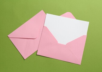 Blank invitation card and envelopes on green background, flat lay. Space for design