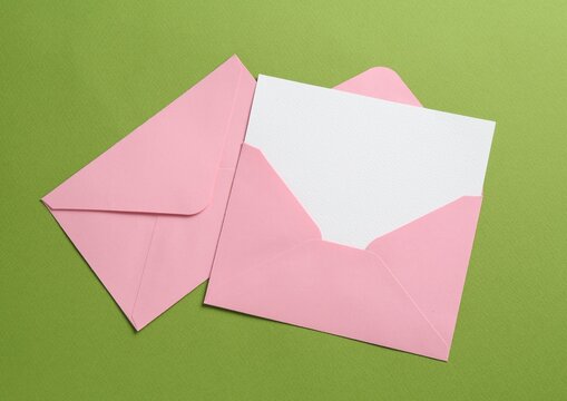 Blank invitation card and envelopes on green background, flat lay. Space for design