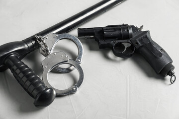 Police baton, handcuffs and gun on light grey table, closeup