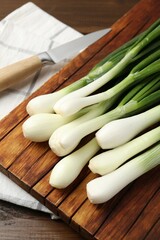Fresh ripe green onions with cutting board and knife on wooden table, closeup