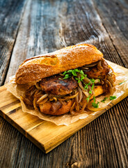 Takeaway sandwich with fried minced cutlets and caramelized onion on wooden table