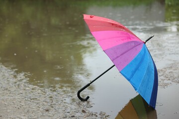 Colorful umbrella on wet asphalt under heavy rain. Space for text