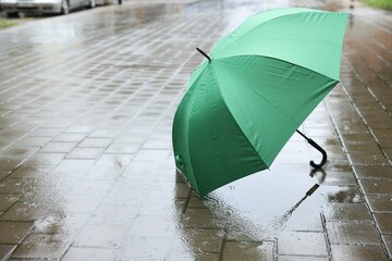 Green umbrella on wet asphalt under heavy rain. Space for text
