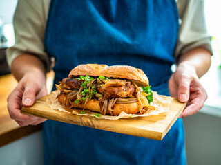 Woman holding wooden board with takeaway sandwich with fried minced cutlets and caramelized onion,...