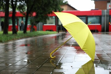 Yellow umbrella on wet asphalt outdoors, space for text