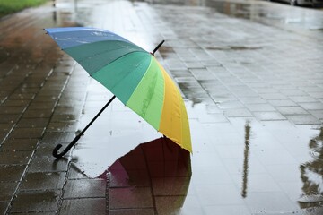 Colorful umbrella on wet asphalt outdoors, space for text