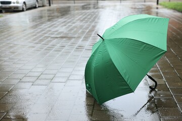 Green umbrella on wet asphalt under heavy rain, space for text
