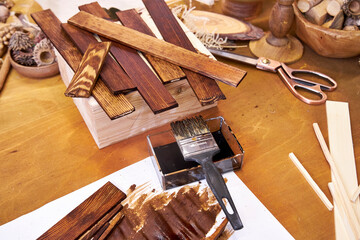 Creative workspace with stained wooden pieces, paintbrush, dried botanicals, and tools. A rustic...