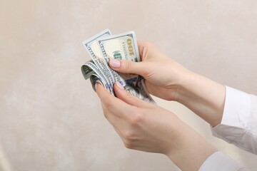 Woman counting dollar banknotes on beige background, closeup. Space for text