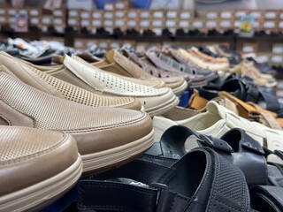 Various men's casual shoes in neutral colors on display in a store. Neatly arranged pairs on shelves with visible price tags in the background