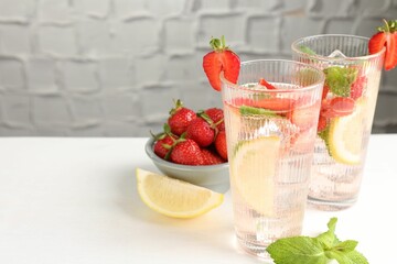 Tasty refreshing drink with strawberries, lemon and mint on white table, closeup. Space for text