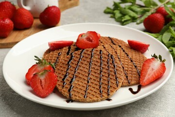 Tasty Dutch waffles (stroopwafels) with strawberries and chocolate sauce on grey textured table, closeup