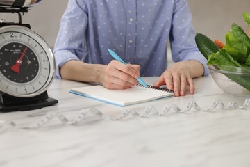 Woman developing diet plan at white marble table indoors, closeup