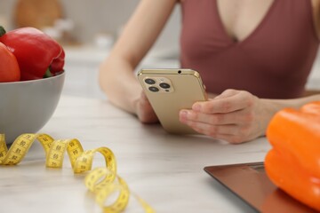 Woman using smartphone at white marble table with vegetables, kitchen scale and measuring tape...