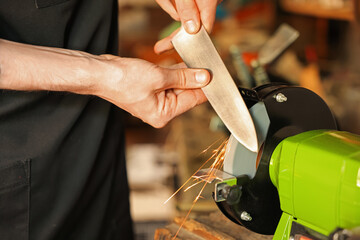 Man sharpening knife with bench grinder indoors, closeup