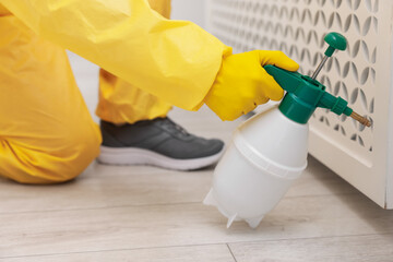 Pest control worker in protective suit spraying insecticide indoors, closeup