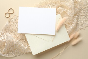 Wedding invitation card, envelope, golden rings, lace ribbon and dry spikes on beige background,...