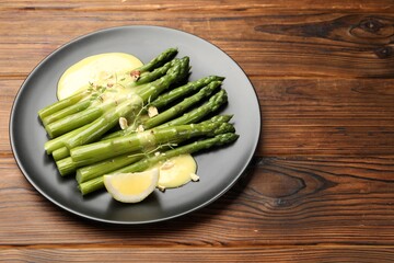 Tasty cooked asparagus served with lemon and sauce on wooden table, space for text