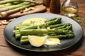Tasty cooked asparagus served with lemon and sauce on wooden table, closeup