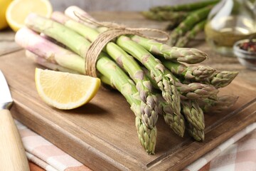 Fresh raw asparagus spears, knife and lemon on wooden table, closeup