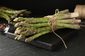 Fresh raw asparagus spears and spices on black table, closeup