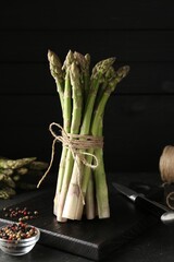 Fresh raw asparagus spears and spices on black table