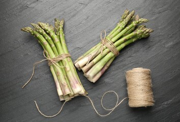 Fresh raw asparagus spears and twine on black table, flat lay